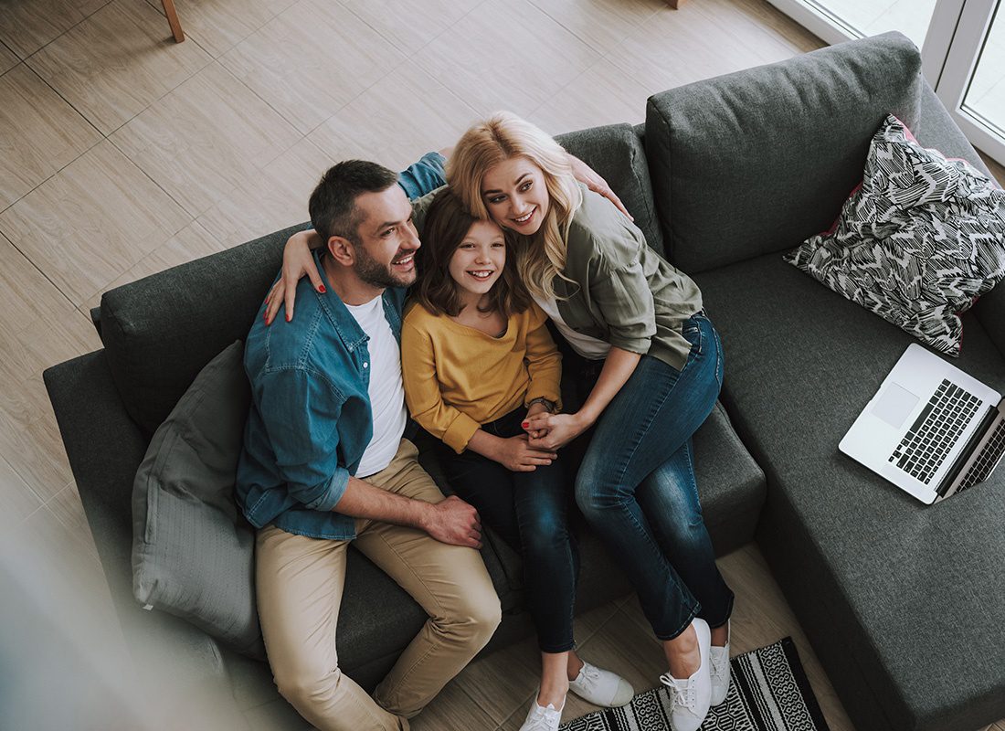 Personal Insurance - Happy Parents Hugging Their Daughter While Sitting on Couch With Laptop